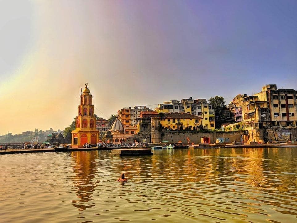 Nashik Godavari River ghats with a historic temple, riverside buildings and calm water during golden hour.